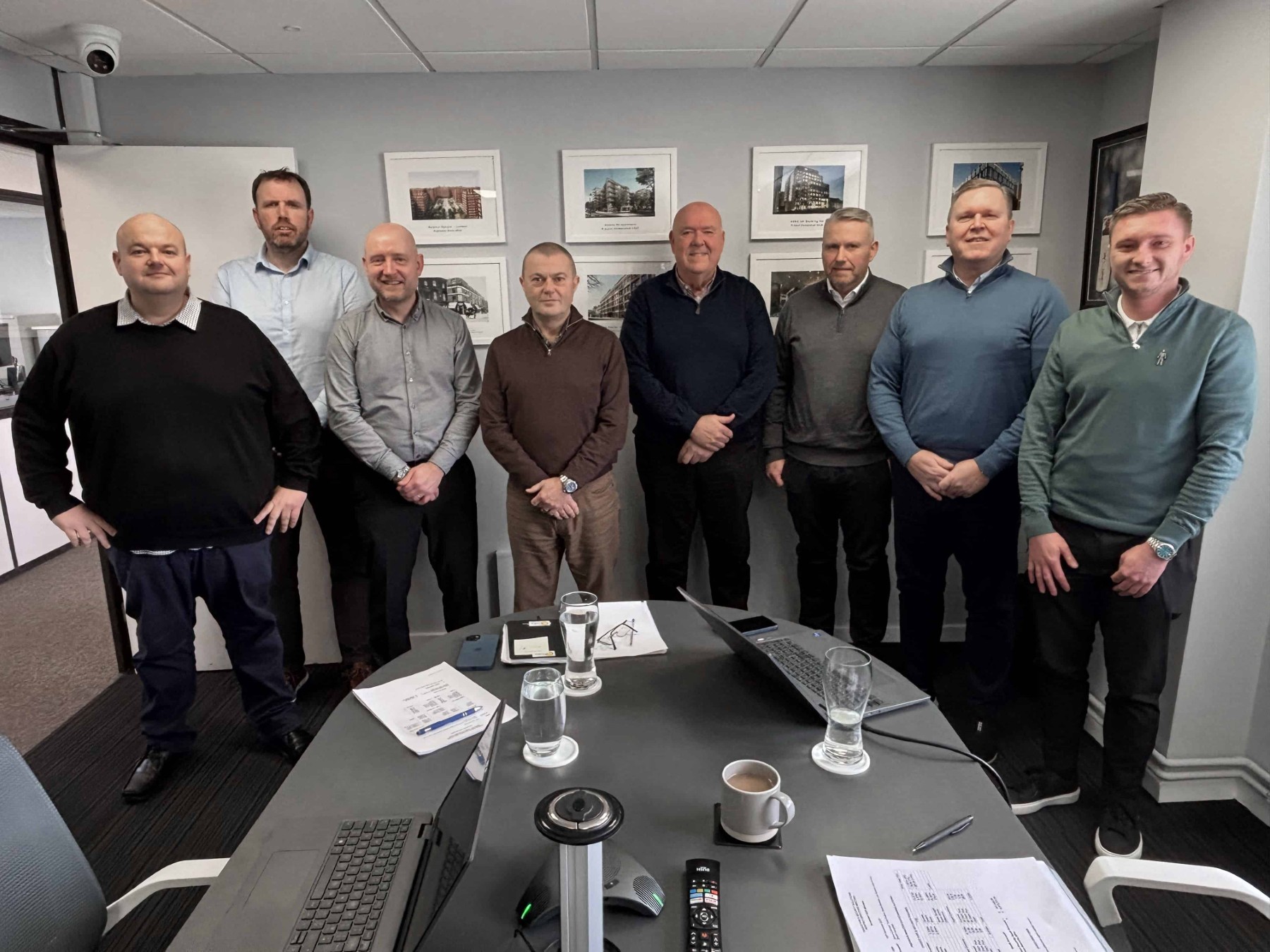 A group of eight men standing in an office conference room, smiling at the camera.