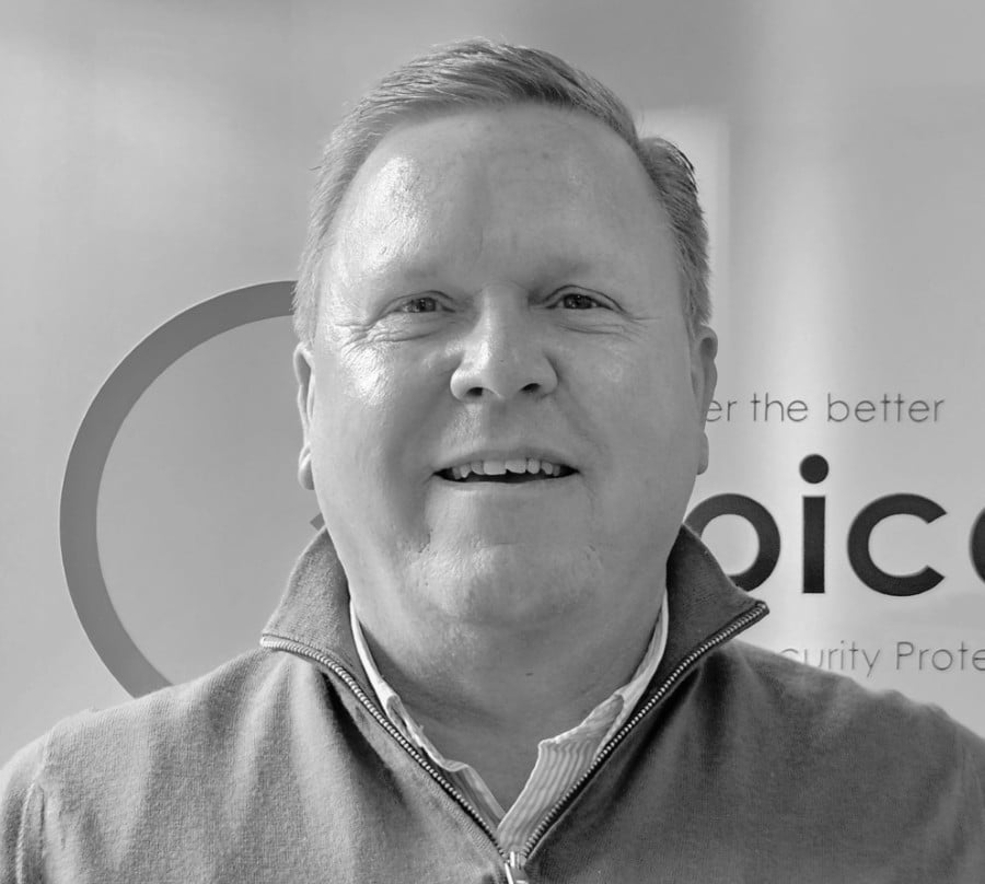 Smiling man in a zip-up sweater poses in front of a partially visible company logo.
