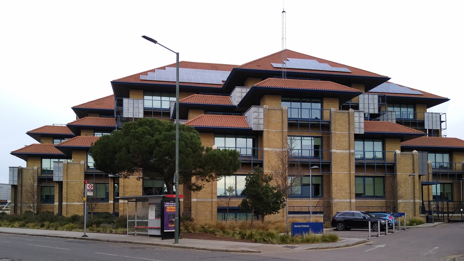 A modern office building with large windows, red roofs, and a bus stop in front.
