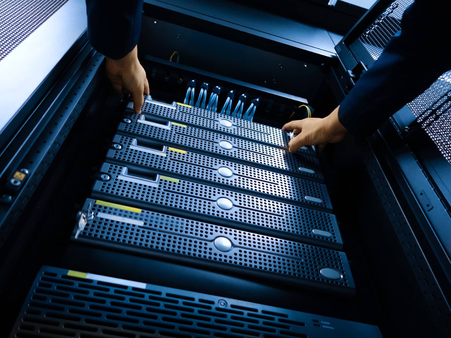 Hands working on server racks inside a data center.