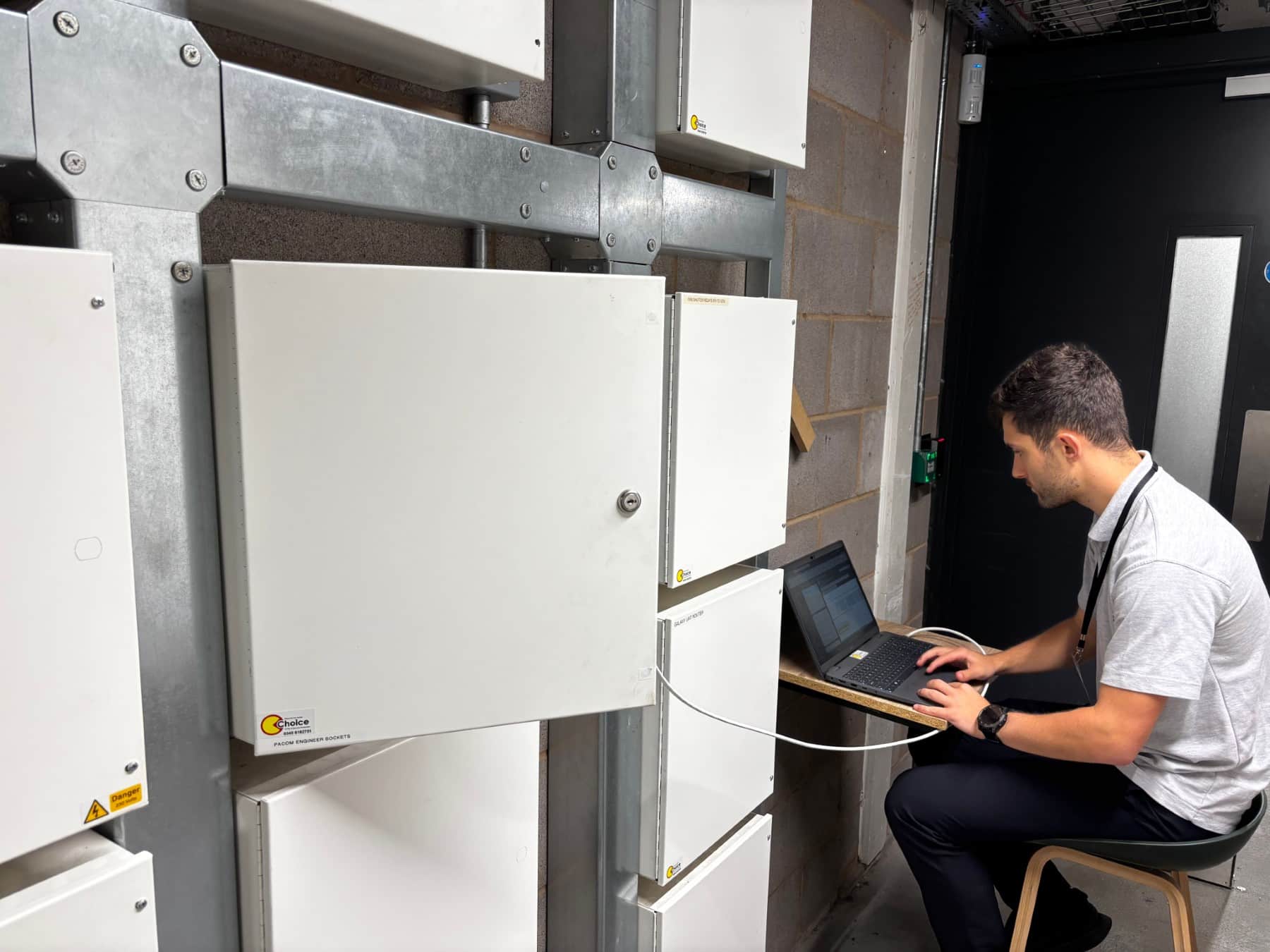 Man working on a laptop connected to alarm system control panels.