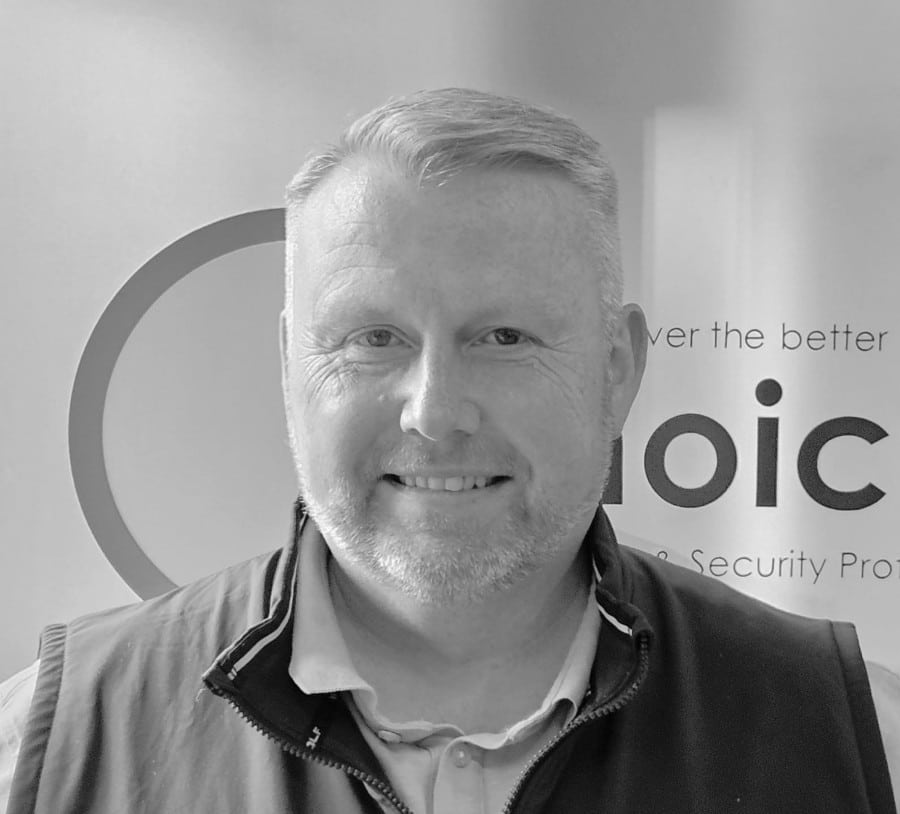 A man smiling in front of a sign, shown in black and white.