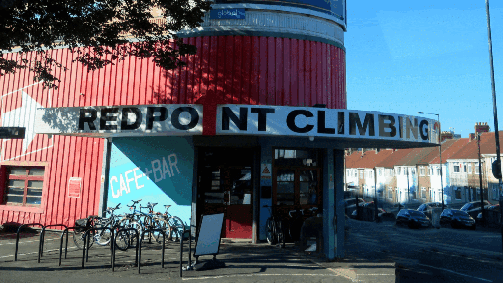 Redpoint Climbing Centre Entrance of a red building with a sign reading "Redpoint Climbing" and several bicycles parked outside.