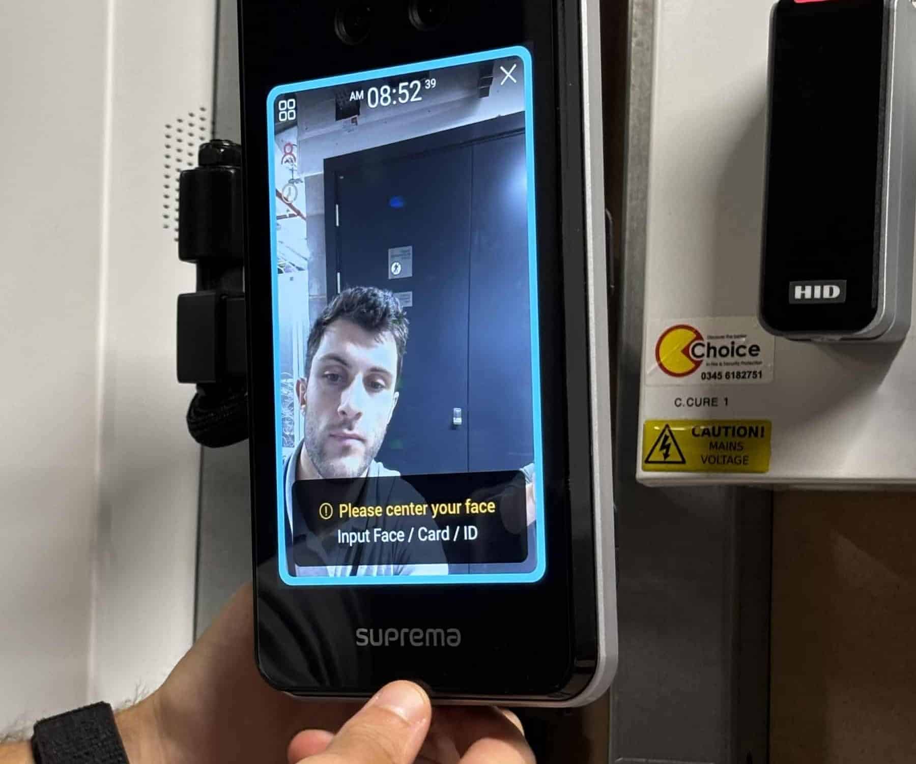 A person uses a facial recognition access control device with a screen prompt to center their face.